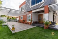 Villa exterior with red-brick and grey stone facade, pergola-covered patio and lawn leading to a wood front door, Hyderabad