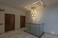 Stair landing with cascading crystal pendant chandelier, walnut chevron doors and glass railing over marble floor, Hyderabad