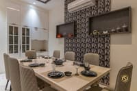 Dining area with six tufted grey chairs, geometric feature wall and white crockery cabinet set for a meal, Hyderabad