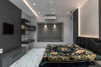 Charcoal-toned bedroom with TV wall, textured backlit niche, floral bedspread and black tufted bed, Hyderabad