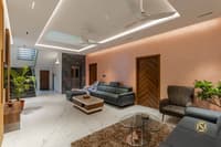 Open living room with peach textured wall, grey leather sofas, glass coffee table and staircase beyond, Hyderabad