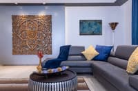 Carved wood mandala panel above a grey leather sectional with navy and yellow cushions and an arc floor lamp, Hyderabad living room