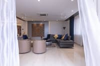 Living room with grey sectional, beige leather swivel chairs and carved wood wall art on a blue accent wall, marble floor, Hyderabad