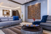Living room with grey sofas, blue velvet cushions and a carved wood medallion on the wall above a round slatted coffee table, Hyderabad