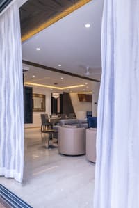 Open-plan living and dining viewed through sheer curtains, crystal chandelier, coffered ceiling and leather swivel chairs, Hyderabad