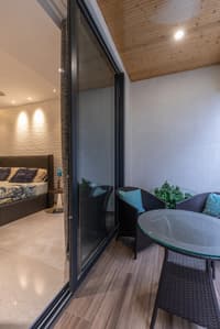 Balcony seating with woven chairs, glass table and wooden ceiling beside a wave-walled bedroom, Hyderabad apartment