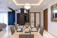 Dining room with light wood table for six, crystal pendant chandelier, navy drapes and a gilded mirror, Hyderabad home