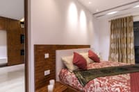 Master bedroom with parquet wood headboard, gold floral drapes and red bolster cushions, Hyderabad home