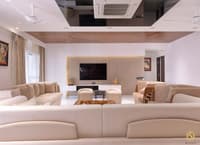 Large living room with cream sectional sofas, wall-mounted TV, fluted wood panel and glossy black ceiling, Hyderabad