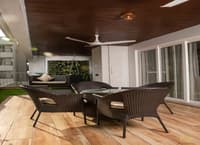 Covered terrace with brown wicker chairs, wood-plank floor, slatted ceiling fan and vertical green wall, Hyderabad