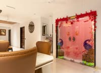 Pooja room with backlit peacock-motif glass doors framed by marigold garlands beside a marble dining nook, Hyderabad