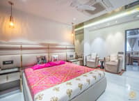 Master bedroom in Hyderabad with tall channel-tufted headboard, pink bandhani bedspread and grey lounge chairs