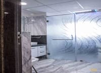 Bathroom with white-and-grey marble walls and floor, frosted etched-glass shower partition and dark vanity, Hyderabad