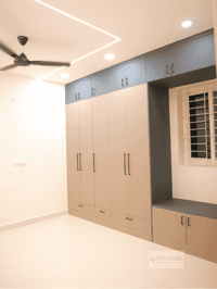 Bedroom wardrobe wall in beige with navy lofts and a cushioned window-seat bench under coffered ceiling, Hyderabad 3BHK