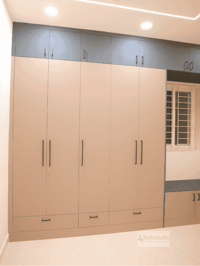 Large beige wardrobe with navy upper loft cabinets and lower drawers beside a window-seat bench, Hyderabad bedroom