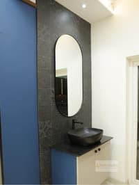 Vanity with black vessel basin, oval mirror, dark patterned-tile feature wall and navy panel, Hyderabad apartment