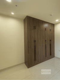 L-corner walnut wardrobe with loft storage and recessed lighting against a pale bedroom wall, Hyderabad