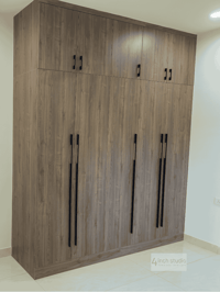 Tall grey-wood wardrobe with overhead loft cabinets and vertical black pulls in a bedroom corner, Hyderabad