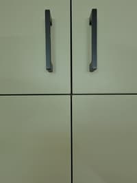 Close-up of off-white cabinet shutters with slim black bar handles and crisp grooved joints, Hyderabad