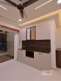 Living-dining storage unit with white cabinets, fluted-glass doors and dark wood backsplash beside a sliding glass door, Hyderabad