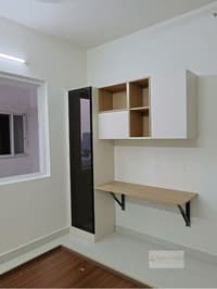 Bedroom study corner with floating wooden desk, open shelf unit and slim tinted-glass tall cabinet by the window, Hyderabad