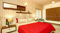 Bedroom in red and cream with patterned accent wallpaper, wood wardrobe and twin bedside lamps, Hyderabad