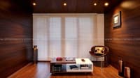 Sitting area with full wood-panelled walls, white venetian blinds, leather sling chair and low storage table, Hyderabad