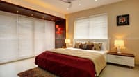 Bedroom in Hyderabad with maroon and beige bedding, white venetian blinds, wood-panelled headboard and twin bedside lamps