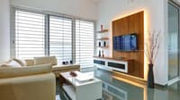 Compact living room in Hyderabad with backlit wood TV panel, beige sofa, white coffee table and louvred windows