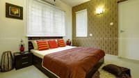 Bedroom with gold damask wallpaper, dark wood bed, orange bolster cushions and white window blinds, Hyderabad