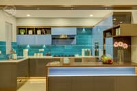 Modern L-shaped kitchen with glossy grey cabinets, blue glass backsplash and a wood breakfast island, Hyderabad