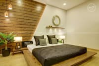 Bedroom with low platform bed, dark quilt and angled wood-clad headboard wall with round mirror and pendant lights, Hyderabad