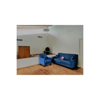 Sparse living room with blue fabric sofa and armchair on light wood flooring against white walls, Hyderabad