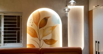 Backlit arched niche with a hand-painted botanical mural of gold and ochre leaves above a leather seat, Hyderabad home