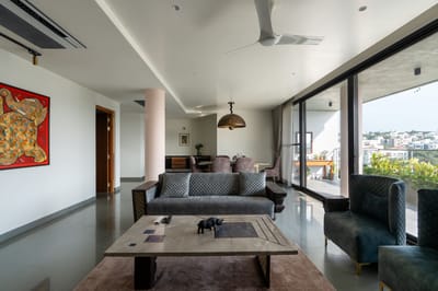Open living room with grey quilted sofas, marble coffee table, bold abstract painting and balcony city views, Hyderabad