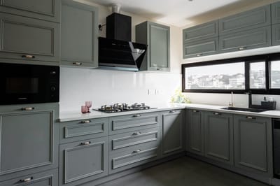 Sage-green shaker kitchen in Hyderabad with black chimney, white quartz counters, gas hob and a city-view window