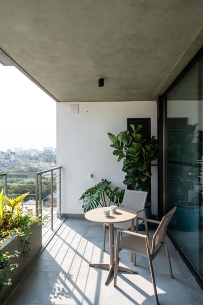 Balcony with bistro table and chairs, fiddle-leaf fig planters and city skyline view under a concrete soffit, Hyderabad