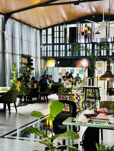 Double-height lounge with green velvet chair, wooden desk and lush palms over terrazzo flooring with black inlay, Hyderabad