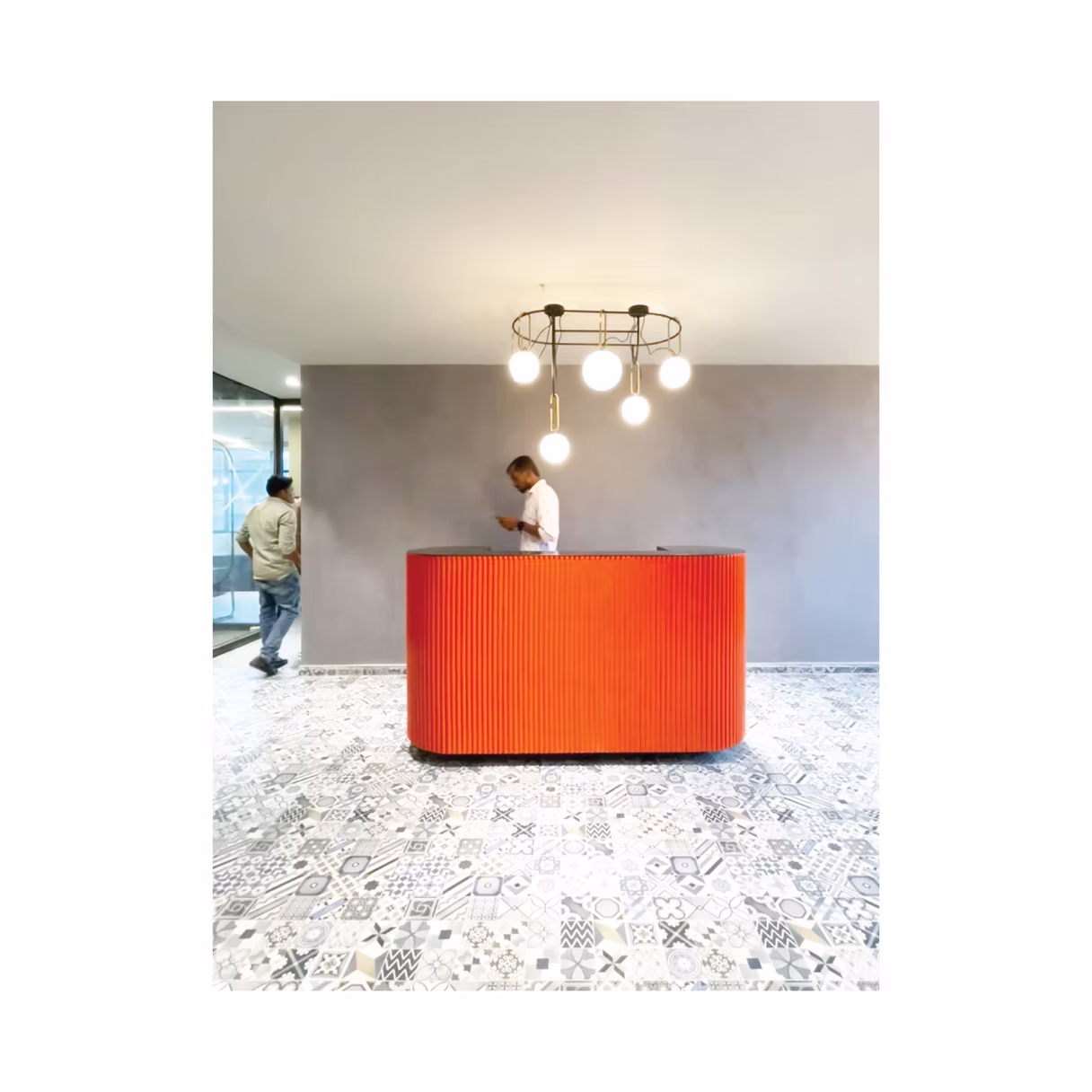 Rounded coral reception desk on patterned cement-tile floor under cluster pendant lights, Hyderabad office interior