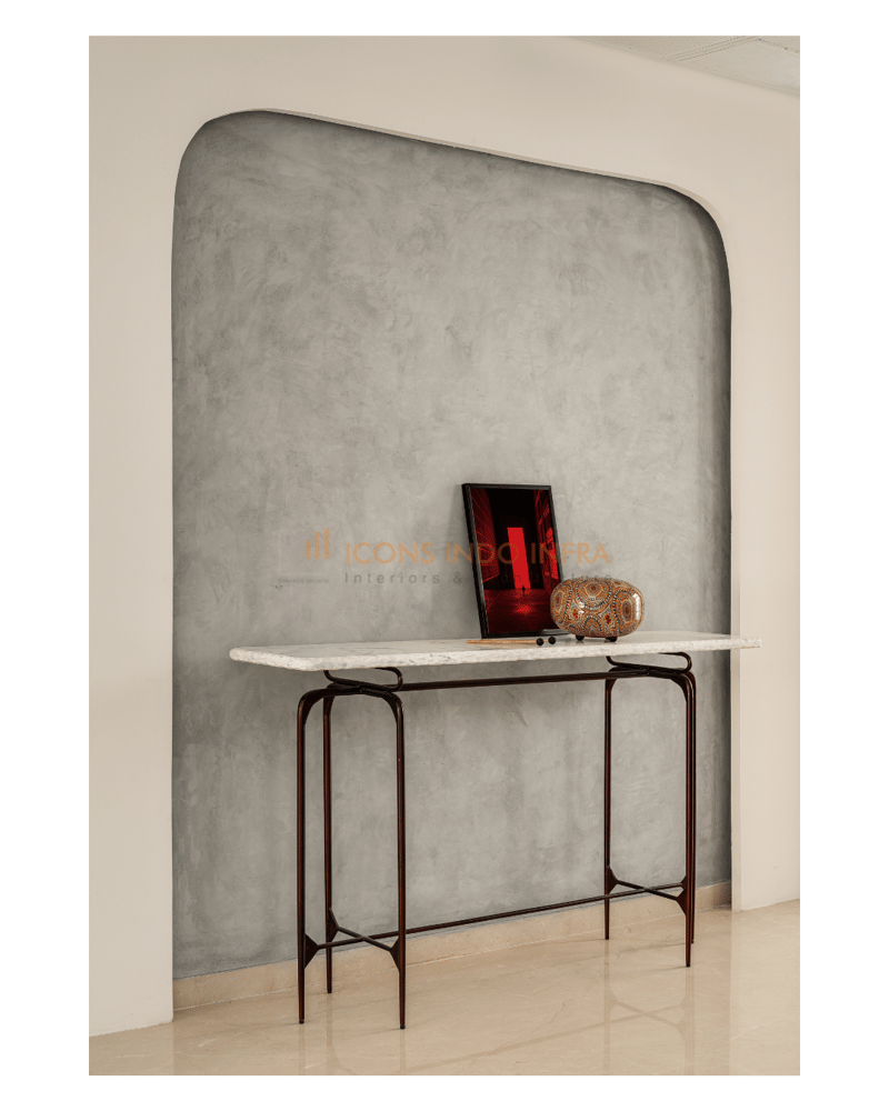 Foyer vignette in Hyderabad with slim metal console table against a textured grey arched plaster wall and decor accents