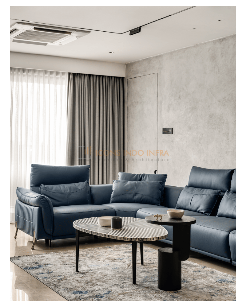 Living room in Hyderabad with deep-blue leather sofa, microcement wall, grey drapes and an oval stone coffee table