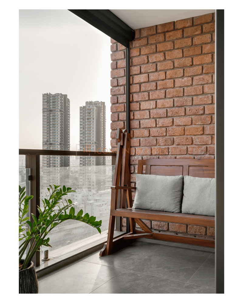 Apartment balcony with exposed brick wall, wooden swing bench in grey cushions and a high-rise skyline view, Hyderabad
