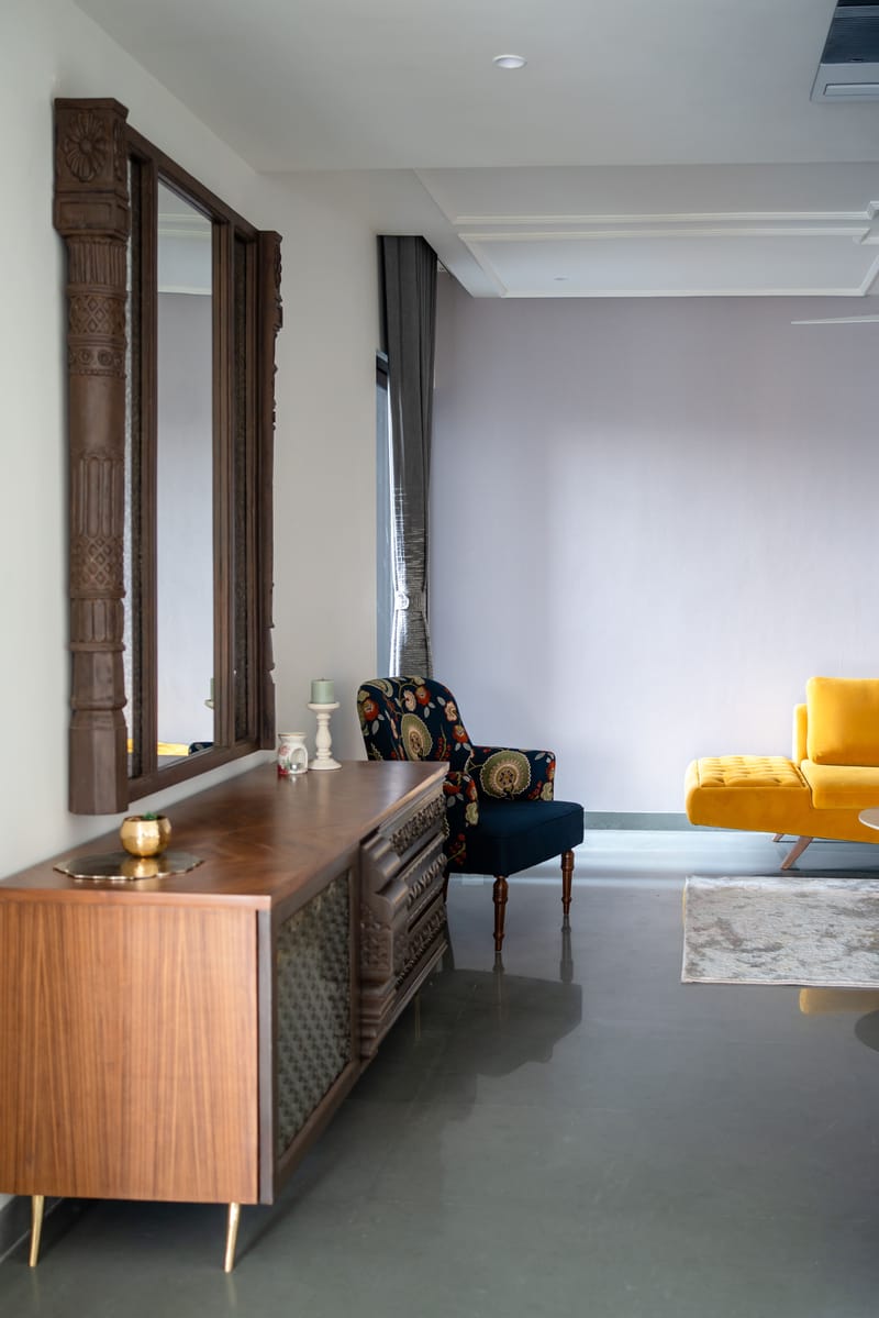 Drawing room console with carved teak sideboard, tall carved-wood mirror, navy floral chair and yellow velvet sofa, Hyderabad
