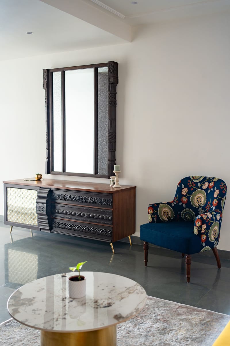 Drawing room corner pairing a carved wood-and-brass console with a navy floral wingback chair and round marble coffee table