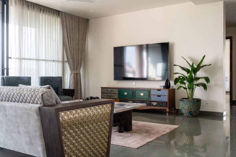 Living room with painted carved console, cane-back grey sofa, draped windows and wall-mounted TV, Hyderabad home