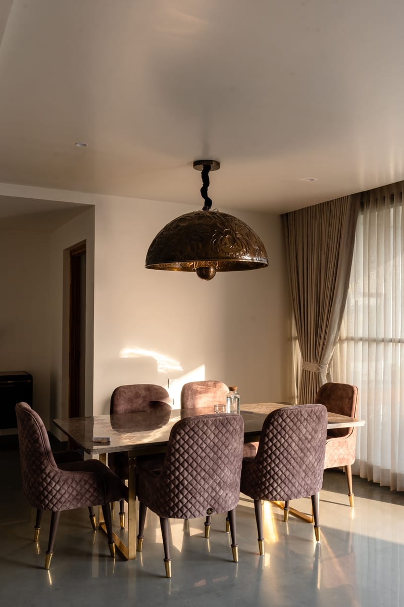 Dining area in Hyderabad with dusty-mauve velvet chairs around a marble table, copper dome pendant and pleated curtains
