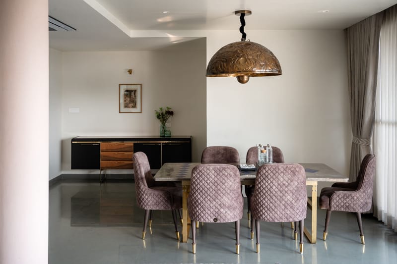 Dining area with marble-top table, mauve velvet tufted chairs and an ornate carved dome pendant light, Hyderabad
