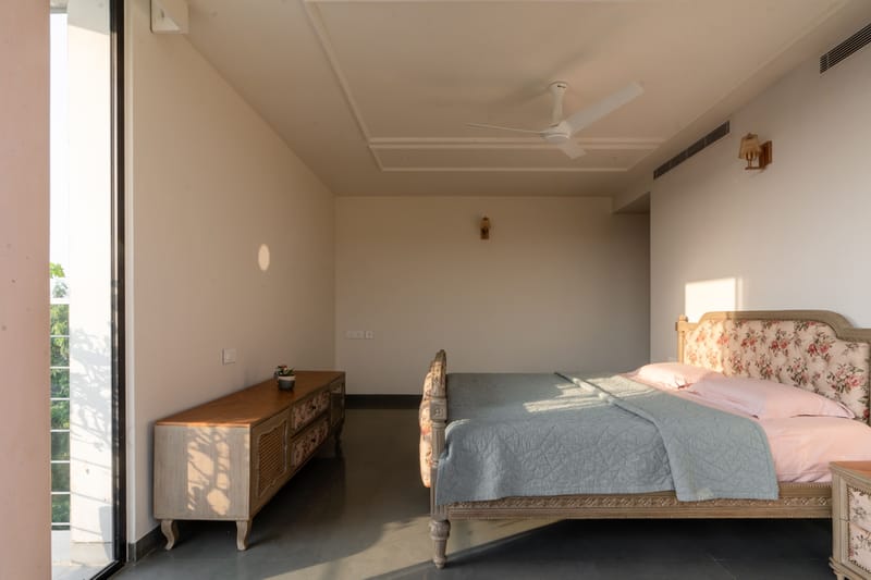 Master bedroom with floral upholstered bed, pink and grey bedding, carved wood console and balcony glass doors, Hyderabad