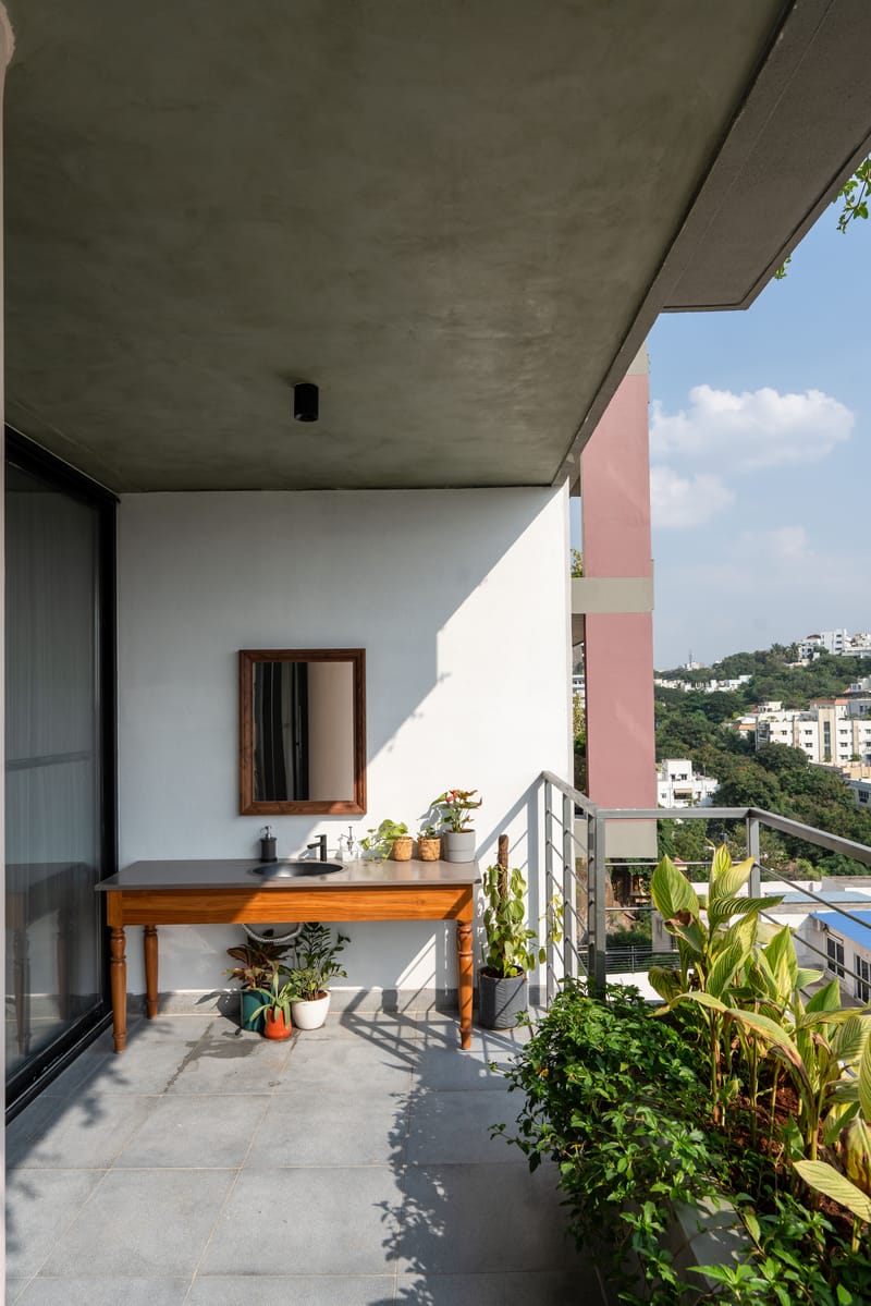 Balcony with wood-framed mirror over a teak console, potted greenery and open city view beyond the railing, Hyderabad