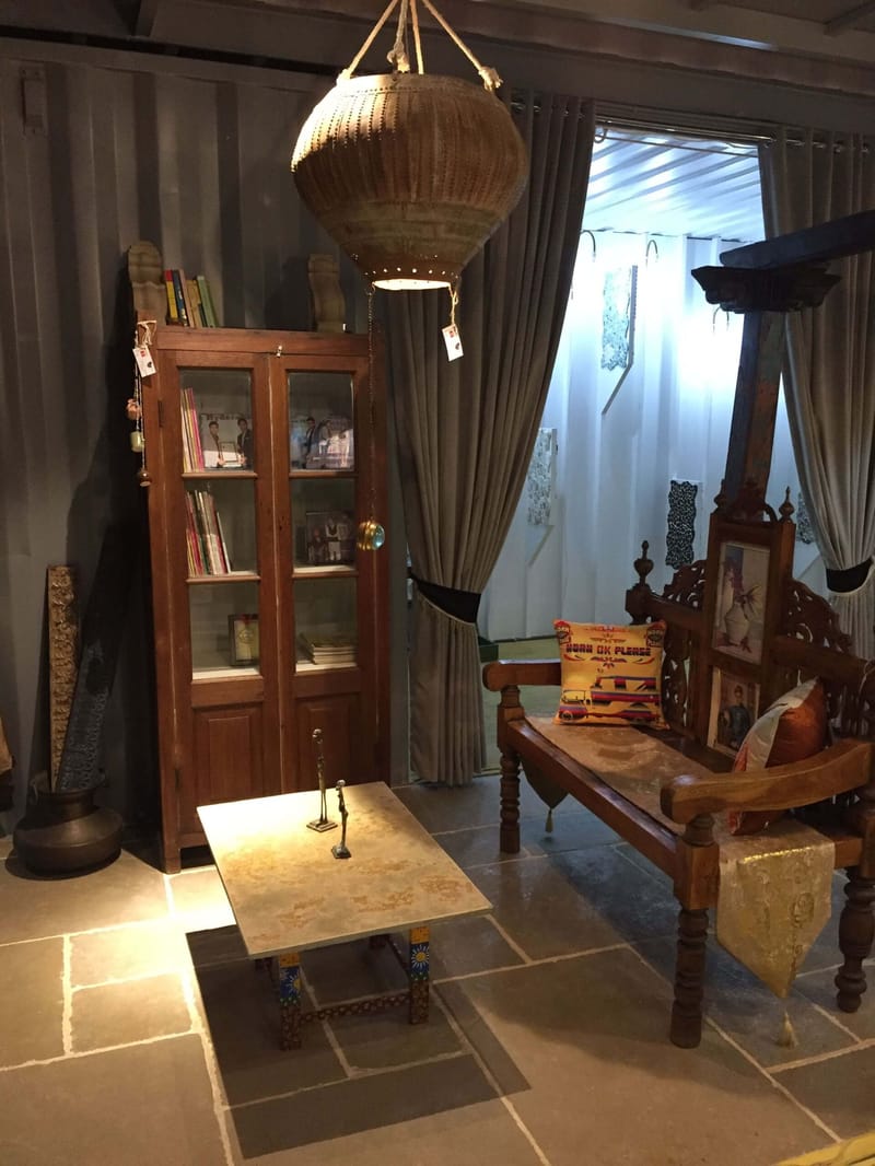 Heritage-style styled corner with carved wooden settee, glass-front bookcase and a woven pendant lamp on stone flooring